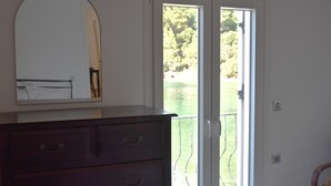 A room with a dark wooden dresser, a mirror, and a sliding glass door leading to a balcony with a view of a lake and trees.