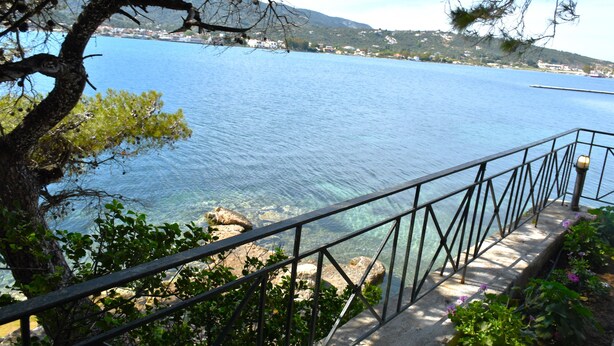 A coastal view with a clear blue sea, a stone pathway, and a metal railing.