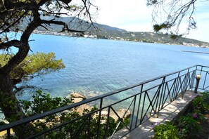 Une vue sur la côte, avec une mer bleue et limpide, un sentier en pierre et une rambarde en métal.