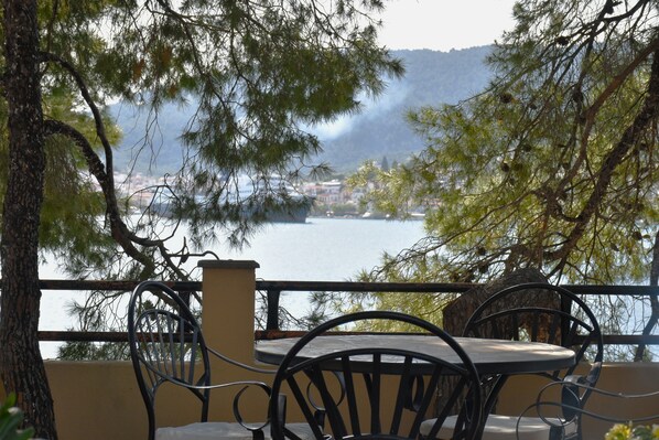 Une terrasse avec une table et des chaises, donnant sur une étendue d’eau et une ville située au loin.