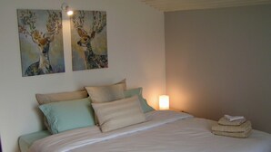 A neatly made bed with a white comforter and pillows, a bedside lamp, and two wall-mounted paintings of deer.