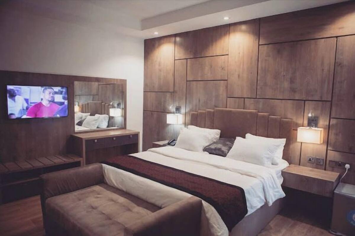 Una habitación de hotel moderna con una cama grande, un televisor montado en la pared y un cabecero de madera.