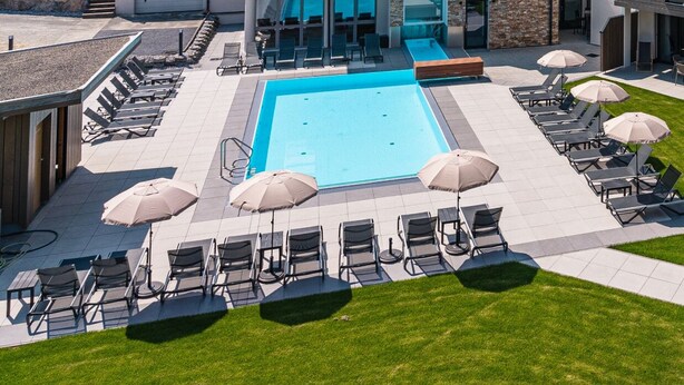 A modern hotel with a swimming pool, outdoor seating, and a view of the surrounding hills.