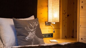 A cozy bedroom with a bed, a nightstand, a lamp, and a wooden wall.