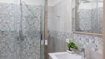 A modern bathroom with a glass-enclosed shower, a white sink with a plant, and a large mirror.