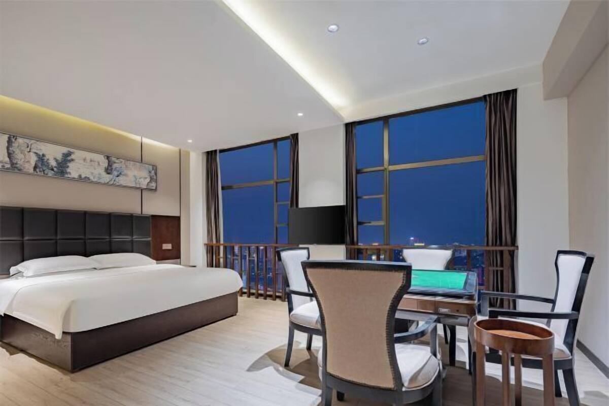 Une chambre d’hôtel avec un lit, un bureau avec un ordinateur portable, une chaise et une grande fenêtre avec des rideaux.