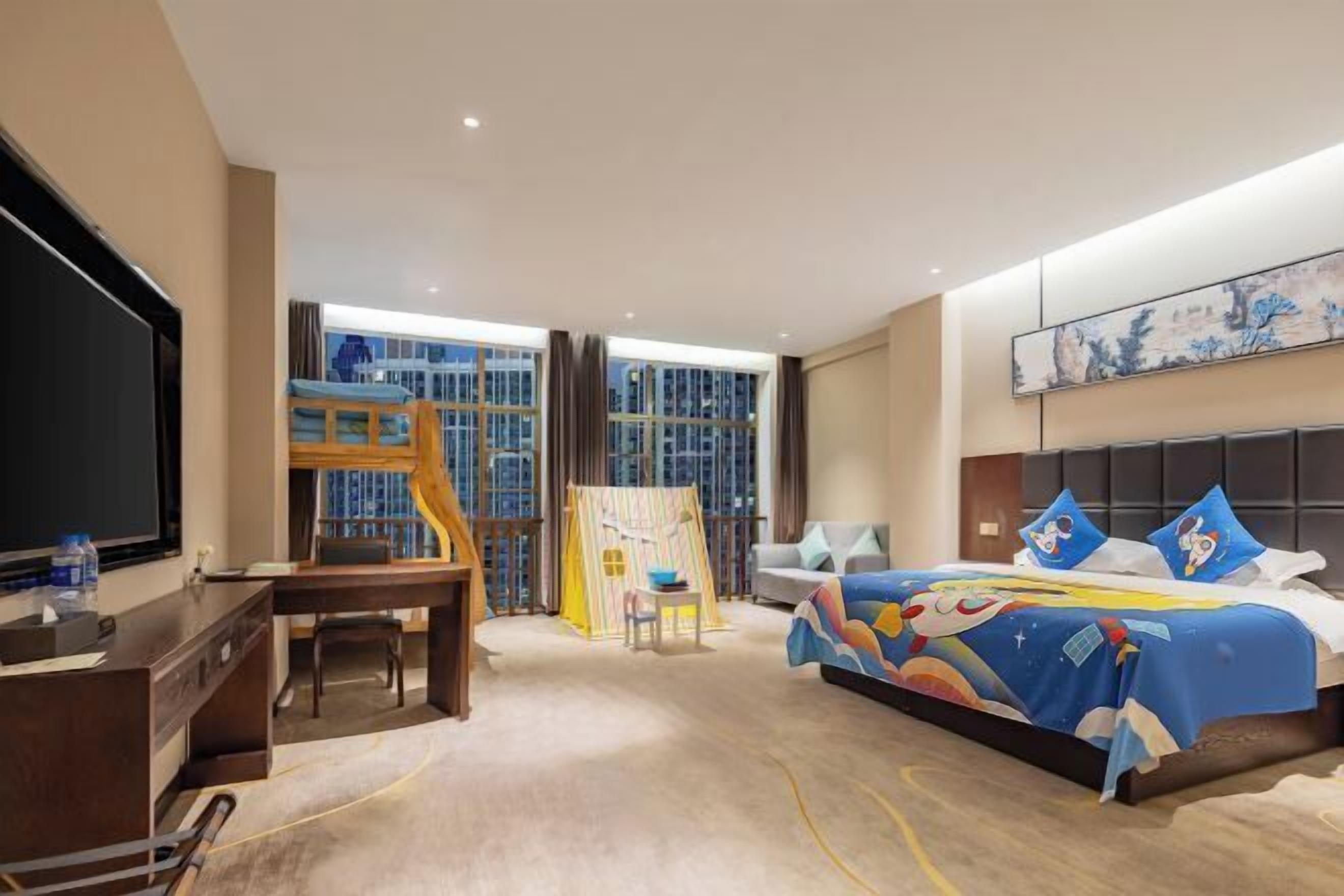 A hotel room with a bed, a desk, a TV, a play area, and a large window.