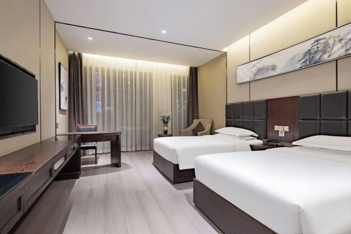 Une chambre d’hôtel avec deux lits, un téléviseur à écran plat, un bureau et une grande fenêtre avec des rideaux.
