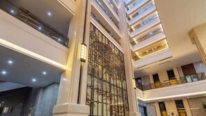 Um átrio com vários níveis, uma coluna decorativa central, guarda-corpos de vidro e um alto teto com claraboias.