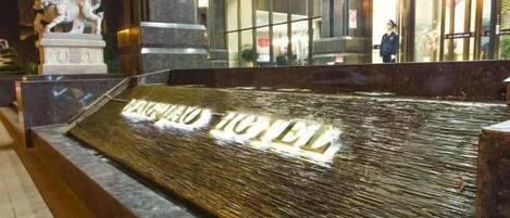 A hotel entrance with a stone statue, a wet floor sign, and a glass facade.