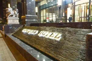 Entrada de hotel con una estatua de piedra, un letrero de piso mojado y un frente de vidrio.