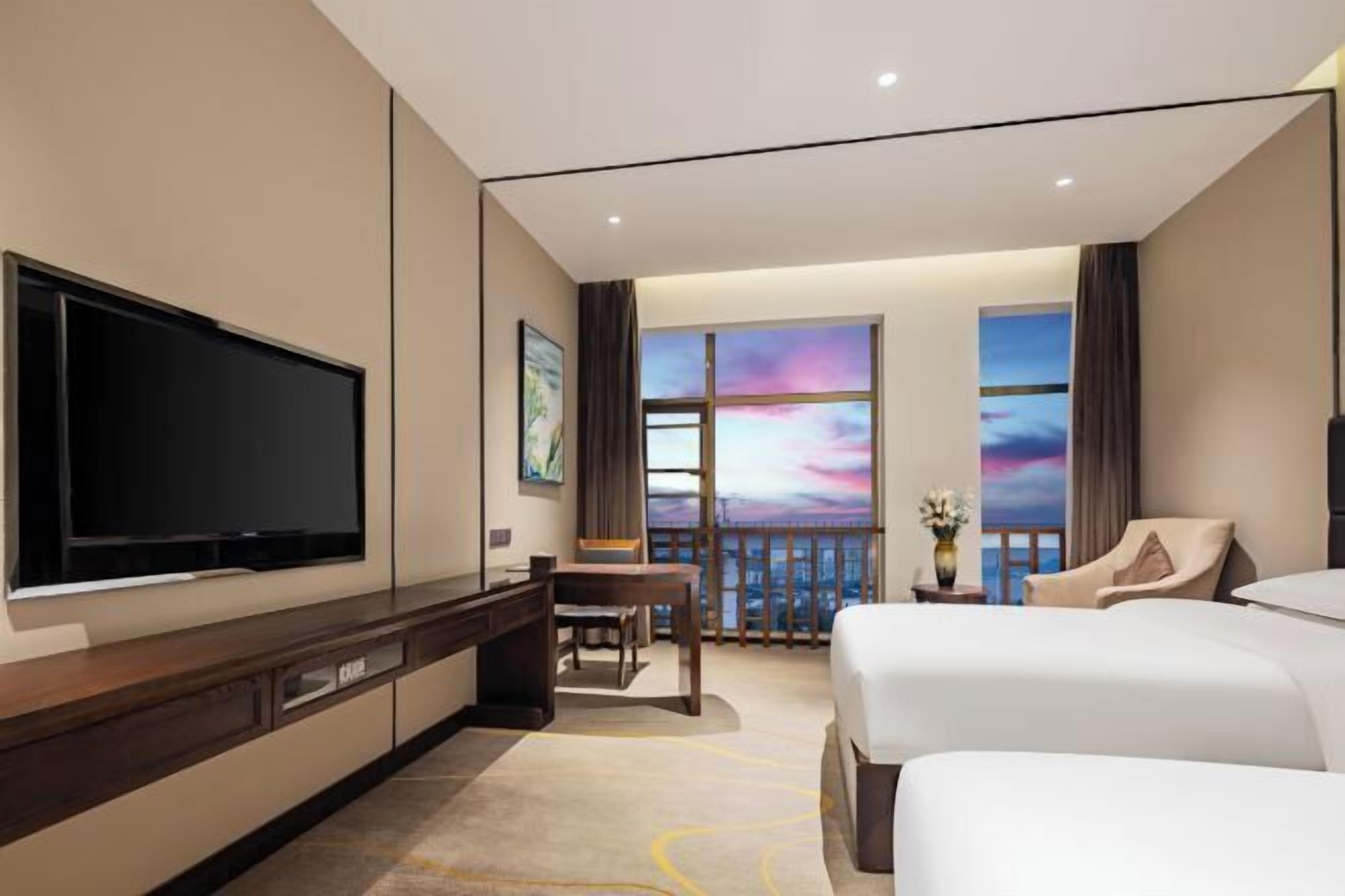 Ett hotellrum med en stor TV, ett skrivbord, två sängar och en balkong med utsikt.