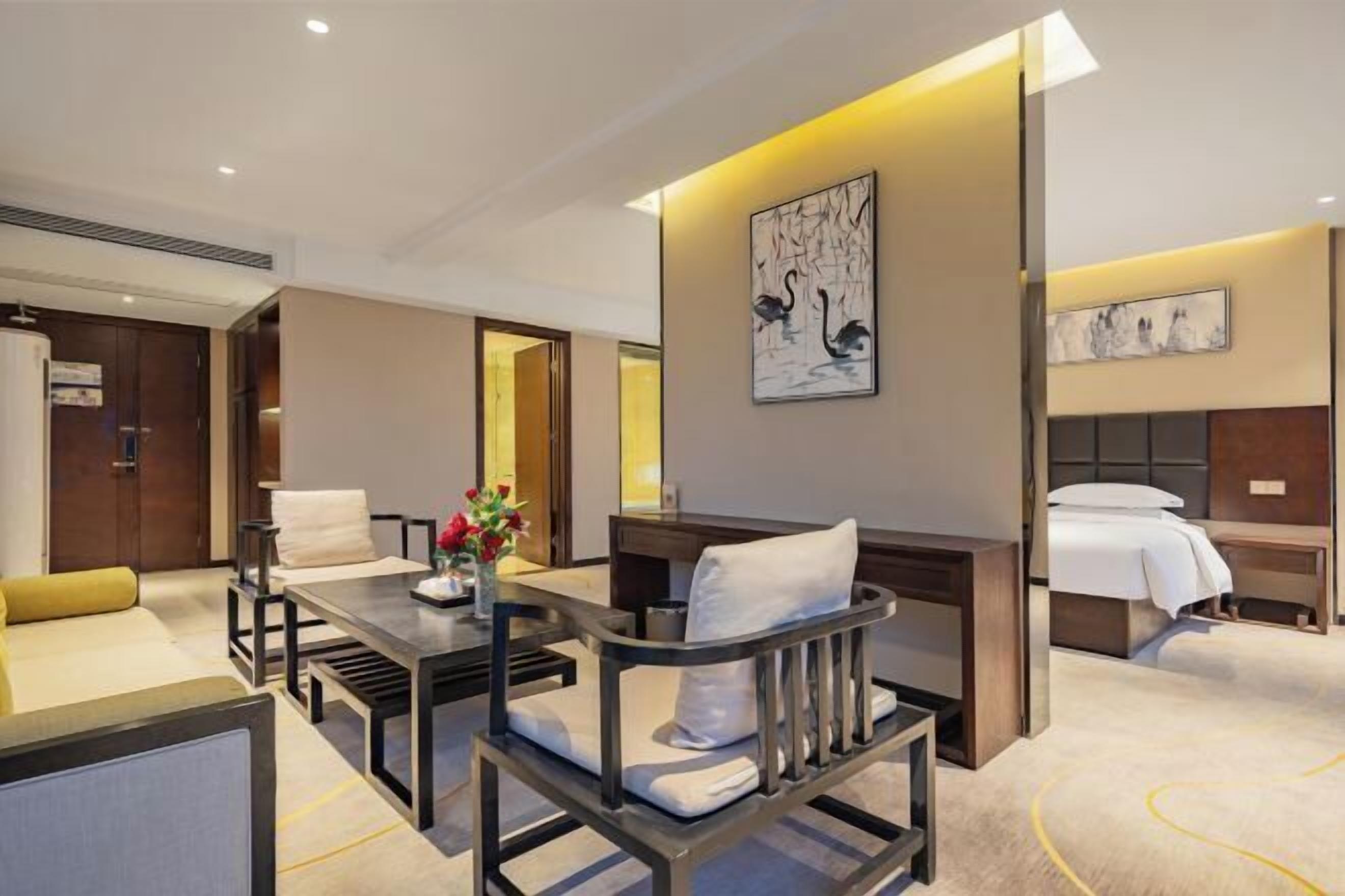 Una habitación de hotel con cama, escritorio, sillón, sofá y obras de arte en las paredes.
