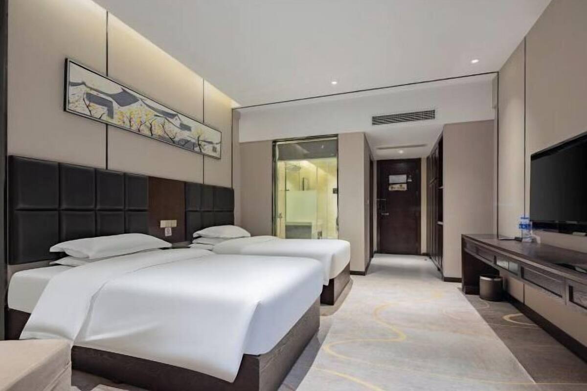 Une chambre d’hôtel avec un grand lit, une télévision, un bureau et une salle de bain visible à travers une porte en verre.