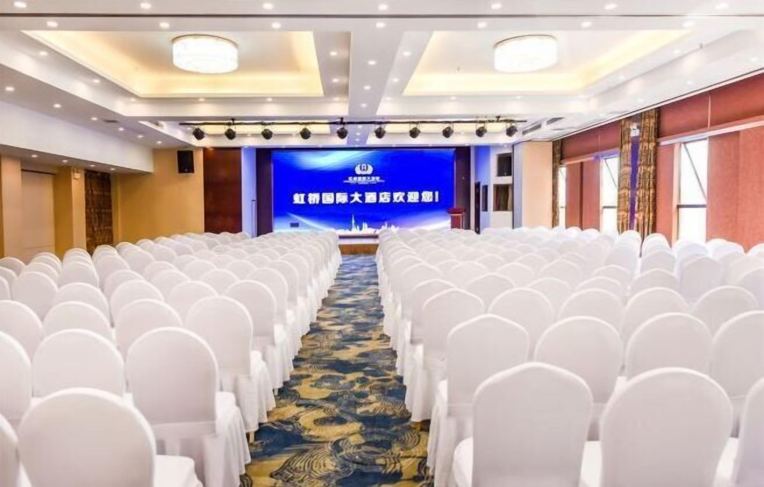 A conference room with rows of white chairs, a blue carpet, and a stage with a blue backdrop.