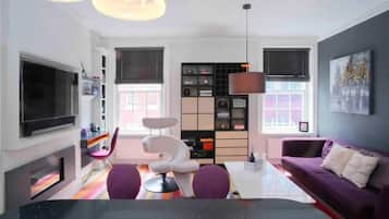 A modern living room with a flat-screen TV, a sofa, a dining table, and a bookshelf.