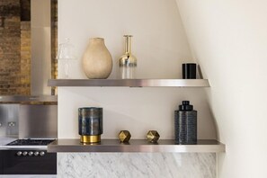 Een keuken met een marmeren aanrechtblad, een roestvrijstalen afzuigkap en een plank met decoratieve objecten.