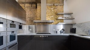A modern kitchen with stainless steel appliances, a brick wall, and a marble countertop. - Penthouse Luxury in Covent Garden (London)