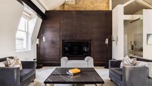A modern living room with dark wood paneling, a fireplace, and two sofas. - Penthouse Luxury in Covent Garden (London)