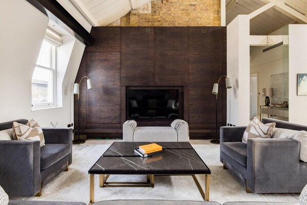 A modern living room with dark wood paneling, a fireplace, and two sofas.