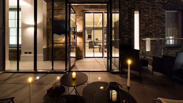 A modern outdoor patio with glass doors leading to a dining area, a fireplace, and a seating arrangement. - Penthouse Luxury in Covent Garden (London)