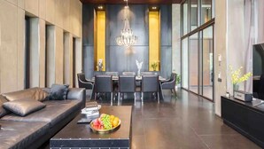 Een moderne woonkamer met een bank, een bijzettafeltje met fruit, een eethoek met stoelen en een kroonluchter.