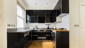 A modern kitchen with black cabinets, a wooden countertop, and a built-in oven. - Designer Muji Home by Harrods (London)