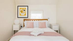 A neatly made bed with a pink blanket and pillows, a framed picture on the wall, and a bedside table with a lamp. - Designer Muji Home by Harrods (London)