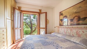 Une chambre avec un grand lit, une fenêtre donnant sur des arbres et un tableau accroché au mur.