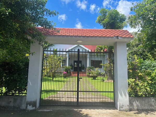 A gated entrance to a building with a red-tiled roof, surrounded by greenery and a well-maintained lawn.