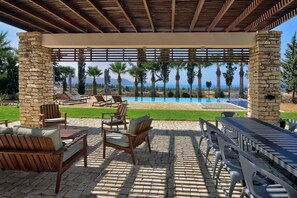 Relax by the pool under a shaded pergola, surrounded by palm trees and mountains.