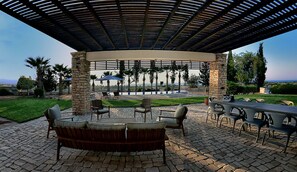 Relax in a tranquil outdoor space with a variety of seating options and a shaded pergola overlooking a landscaped garden and pool.
