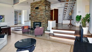 A spacious living area with a stone fireplace, modern furniture, and a staircase leading to an upper level. - Incredible Large Villa, Paphos, 6 bedrms BBQ Huge Pool Childrens pool Quiet area (2CQW+J39 Poli Crysochous, Cyprus)