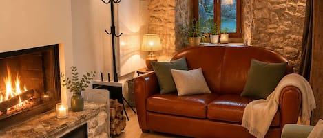 A cozy living room with a fireplace, a leather sofa, a coffee table with candles, and a stone wall.