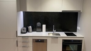Una cocina moderna con armarios blancos, salpicadero negro y pileta de acero inoxidable.