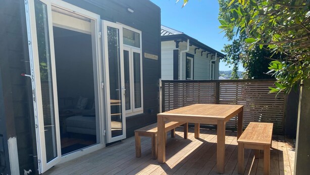 Una terraza de madera con una mesa, bancos, un ventanal corredero y una valla de madera.