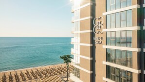 Un edificio de hotel con vista a la playa, llamado 'GRIFID NOA', y una fila de sombrillas de playa al frente.