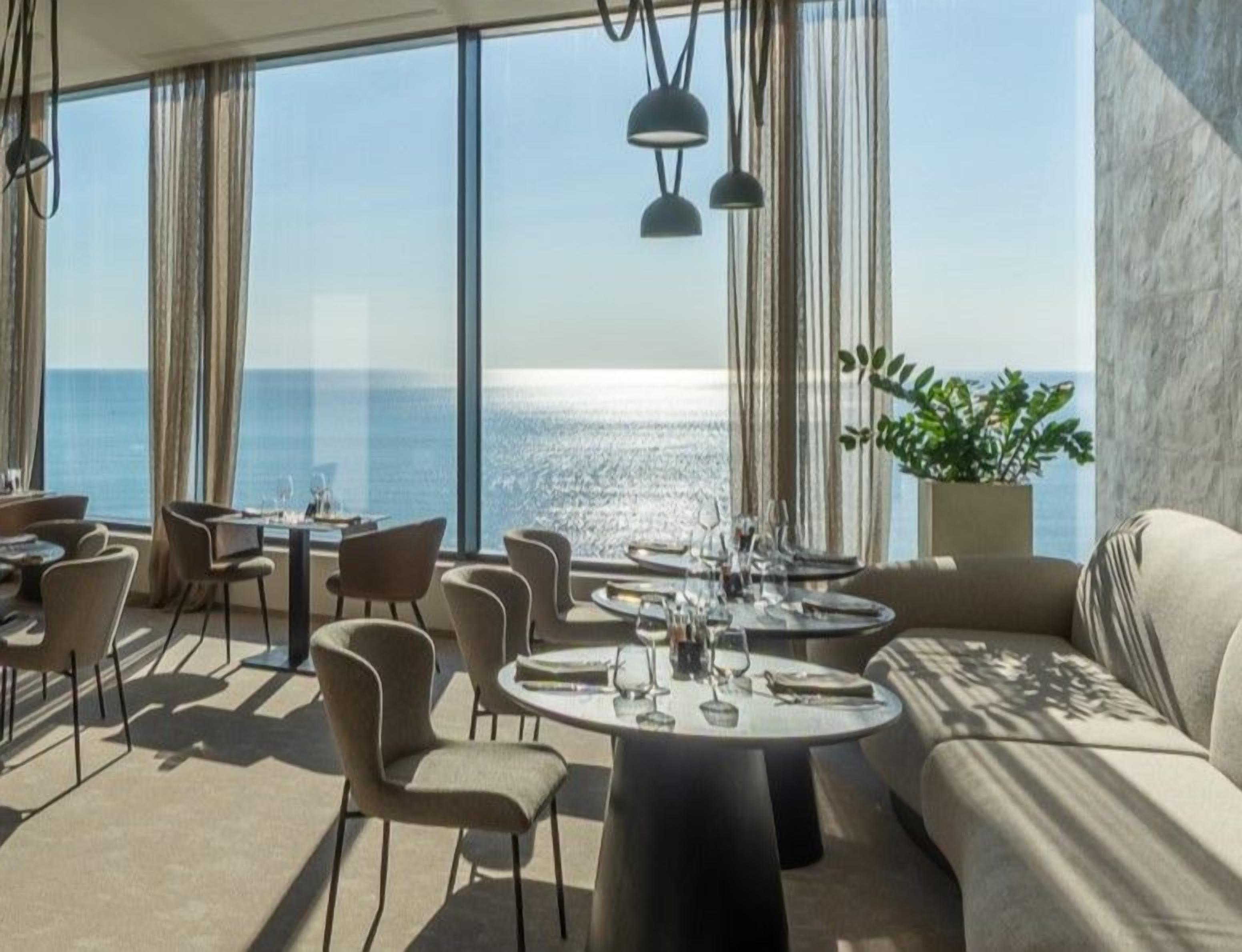 A dining area with round tables, chairs, and a view of the sea.
