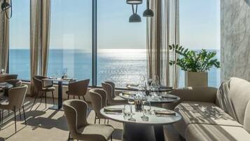 A dining area with round tables, chairs, and a view of the sea.