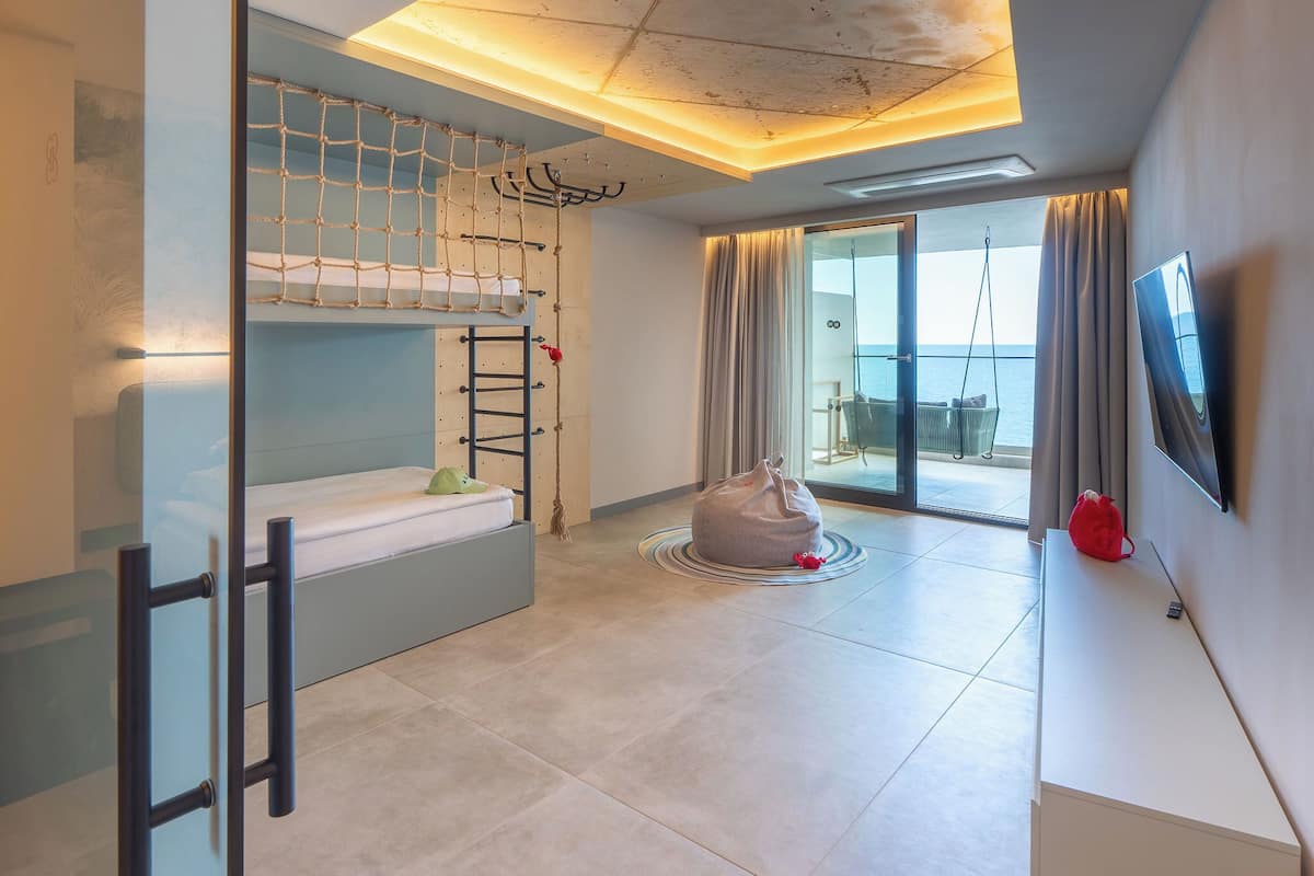 Una habitación moderna con literas, un sillón de mimbre, televisión y vista al mar.