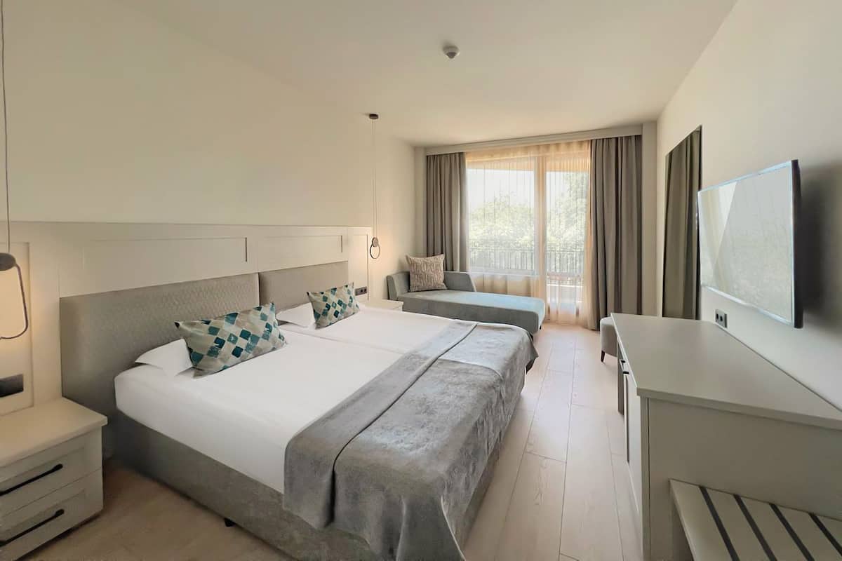 Habitación de hotel con una cama grande, un escritorio, un televisor y una ventana con cortinas.