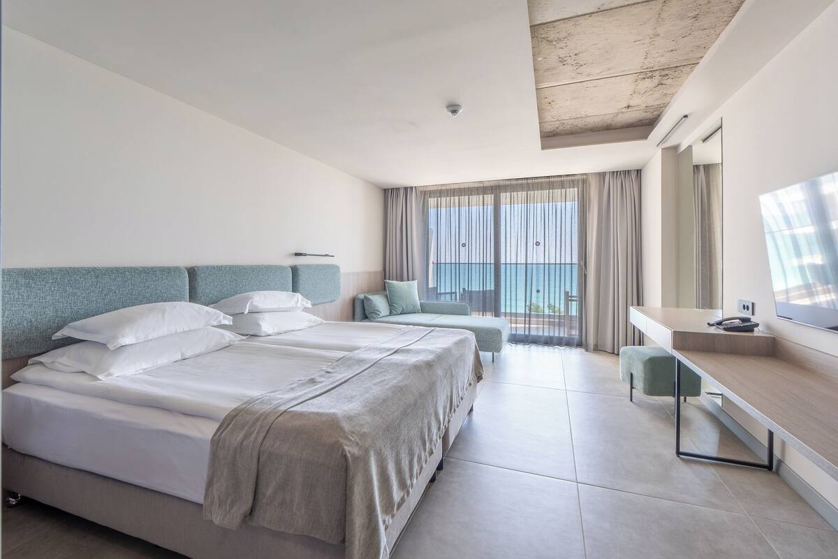 Habitación de hotel con dos camas, un escritorio, una silla y un ventanal con cortinas.