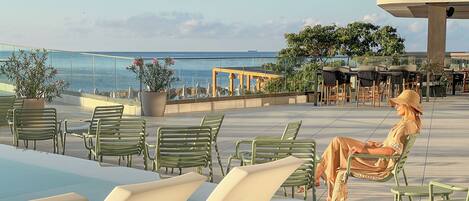 A rooftop terrace with seating areas overlooking the sea, potted plants, and outdoor furniture.