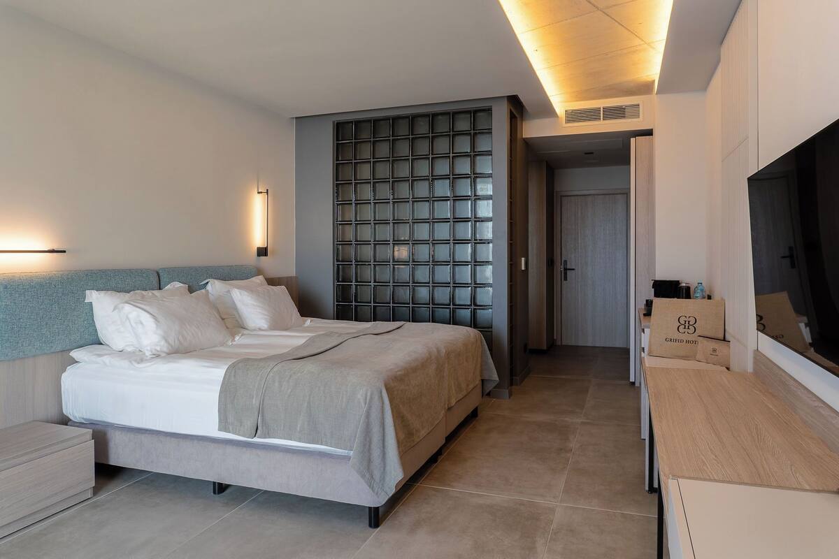 Un dormitorio moderno con una cama grande, cabecera empotrada, televisor de pared y mesita de noche de madera.