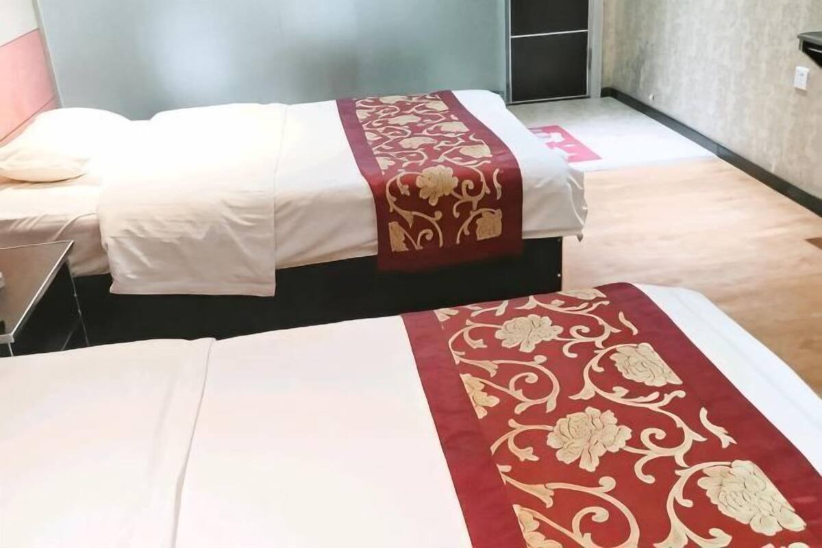 Zwei Betten mit roten und goldenen Tagesdecken, ein kleiner Tisch und ein Wandregal.