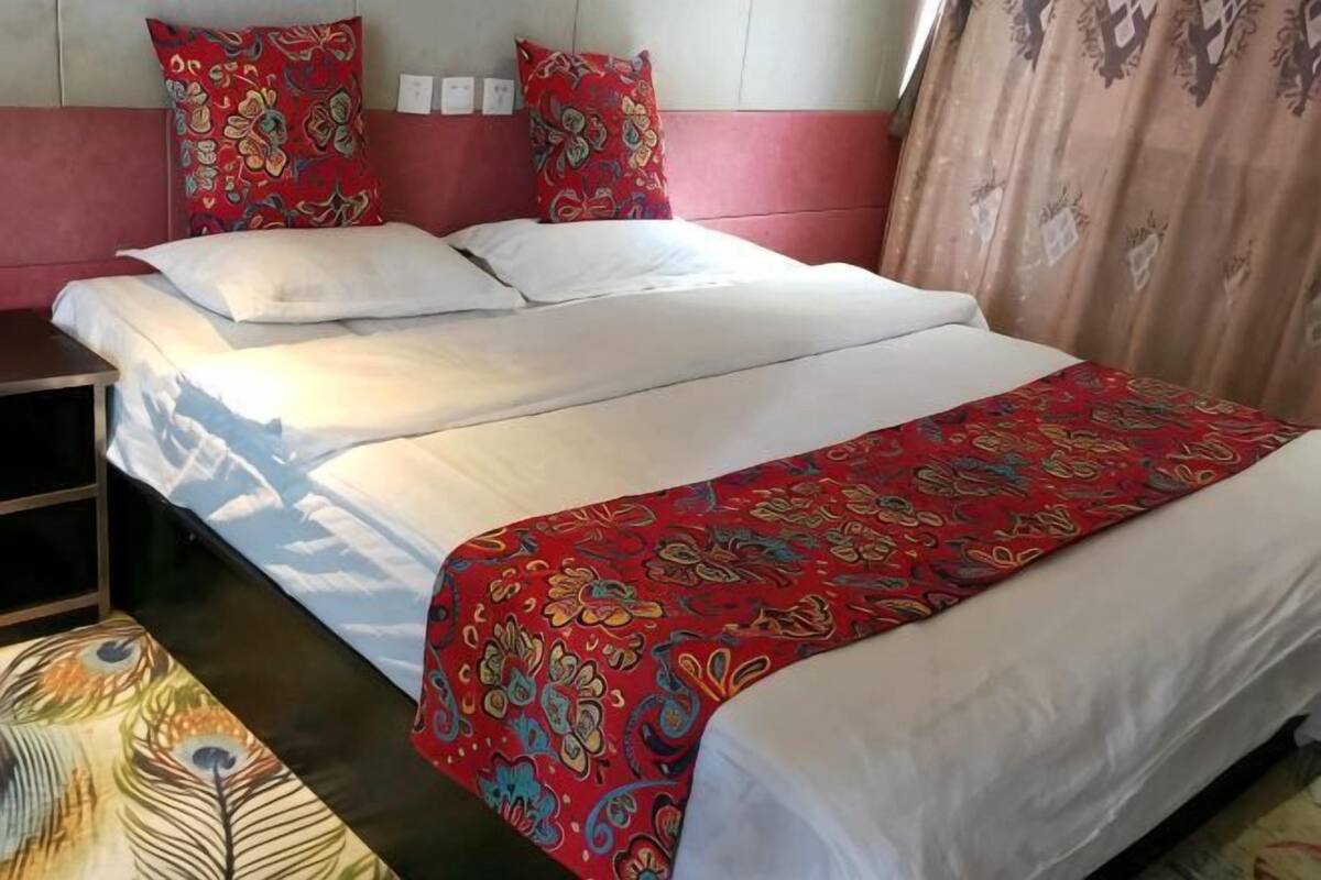 Ein Bett mit rotem, gemustertem Bettbezug, einem weißen Kopfkissen und einer roten Kopfteil.