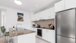 A modern kitchen with white cabinets, a stainless steel refrigerator, a microwave, and a sink.