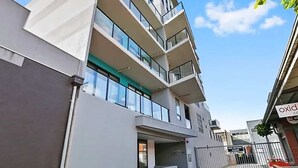 A multi-story building with balconies, a gated entrance, and a clear sky.