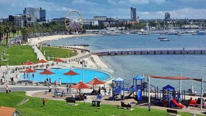 A waterfront park with a swimming pool, playground, and a Ferris wheel in the background.