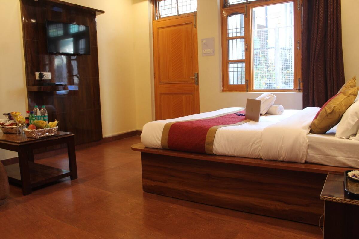 Una habitación de hotel con cama, escritorio, televisión y ventana con cortinas.